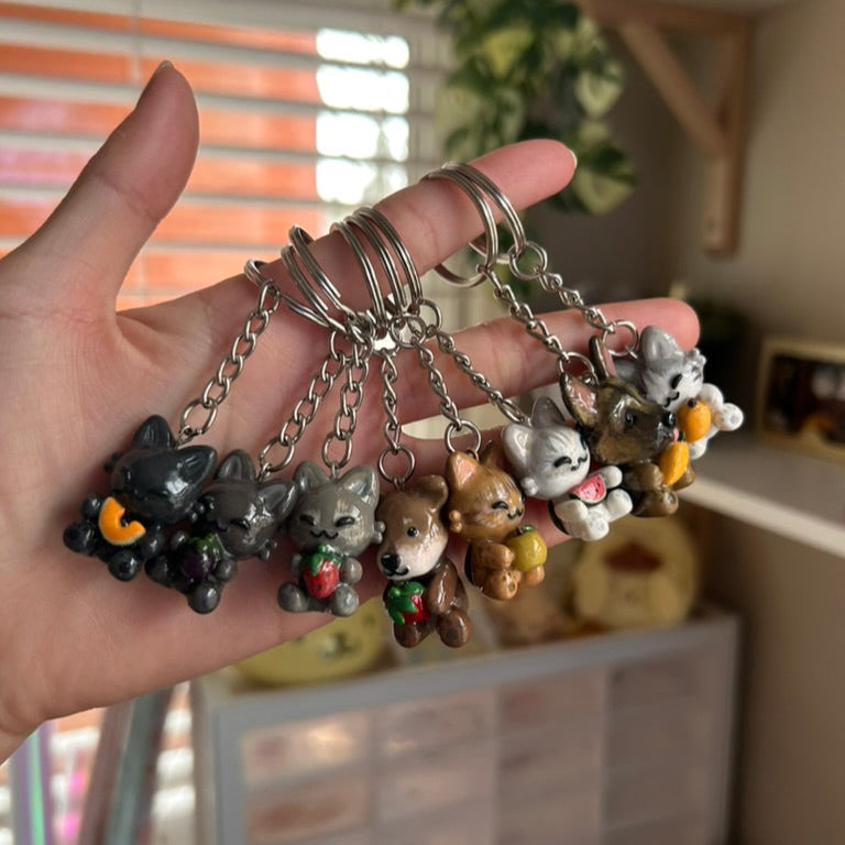 Hand holding a collection of small animal figurine keychains with a blurred indoor background.